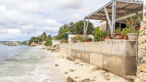 A coastal view with a concrete wall, potted plants, and a building with a wooden roof. - Kasita di Mama (Kralendijk)