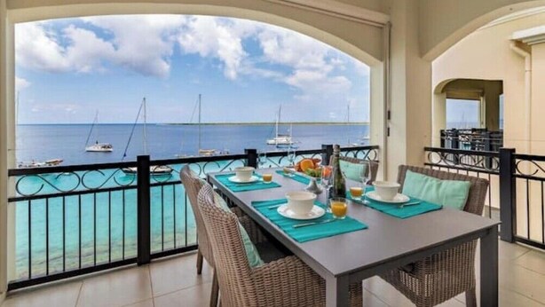 Un coin repas offrant une vue sur la mer, avec une table dressée, comprenant des assiettes, des verres et une bouteille.