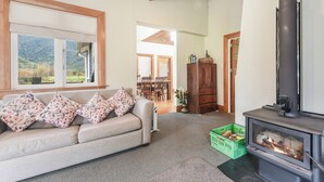 A cozy living room with a sofa, a fireplace, and a view of the outdoors. - Fantail Cottage Kaiuma Bay - Havelock Holiday Home (Havelock)