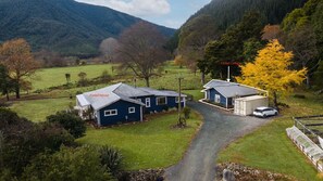 Een landgoed met een blauw huis, genaamd 'Fantail House', een kleiner blauw gebouw met de naam 'Fantail Cottage', en een witte auto geparkeerd nabij de cottage.