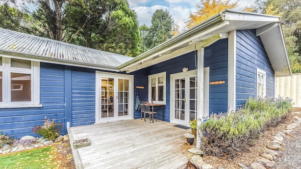 A blue house with a wooden deck, a covered porch, and a garden with plants and rocks. - Fantail Cottage Kaiuma Bay - Havelock Holiday Home (Havelock)