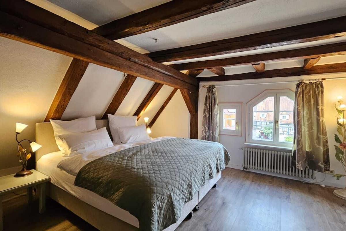 Een slaapkamer met een bed, nachtkastje, raam met gordijnen en een radiator.