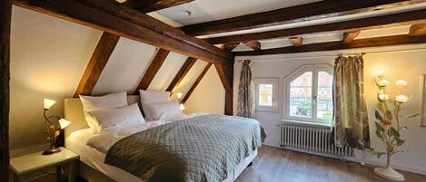 A bedroom with a bed, a nightstand, a window with curtains, and a radiator.