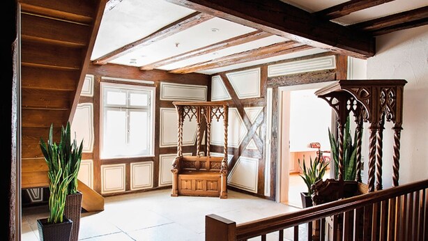 Una habitación amplia con techo alto, vigas de madera a la vista, un ventanal grande y una cama con dosel de madera.