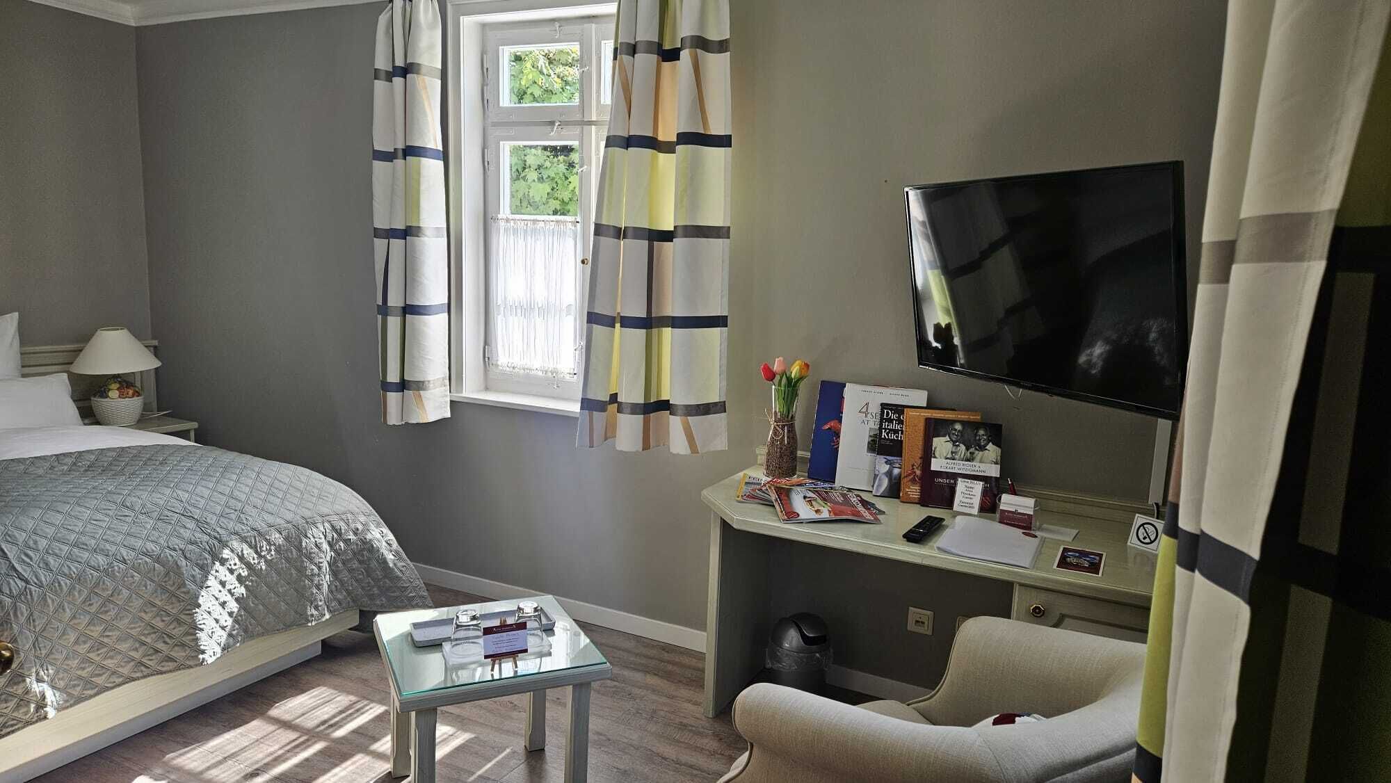 Une chambre d’hôtel avec un lit, un bureau avec une télévision, une chaise et une fenêtre avec des rideaux.
