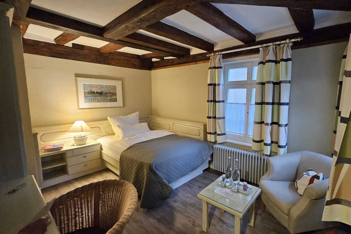Een gezellige slaapkamer met een bed, nachtkastje, lamp, stoel en een radiator.