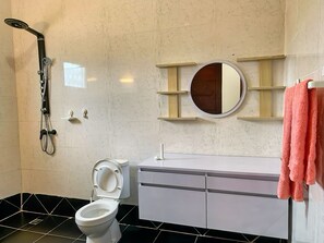 Een badkamer met een wit toilet, een douche, een wastafel met een spiegel en een handdoekrek.