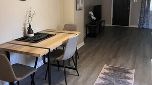 Ein Essbereich mit Holztisch, Stühlen, einer Vase mit Ästen, einem Gemälde und einem Fernseher auf einem Schrank.