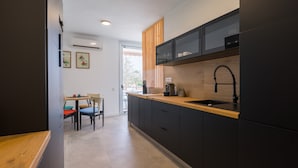 A modern kitchen with dark cabinetry, a wooden countertop, and a black faucet. There is a dining area with a table and chairs visible in the background. - Apartment in Gran Canaria Near Maspalomas Dunes (San Bartolomé de Tirajana)