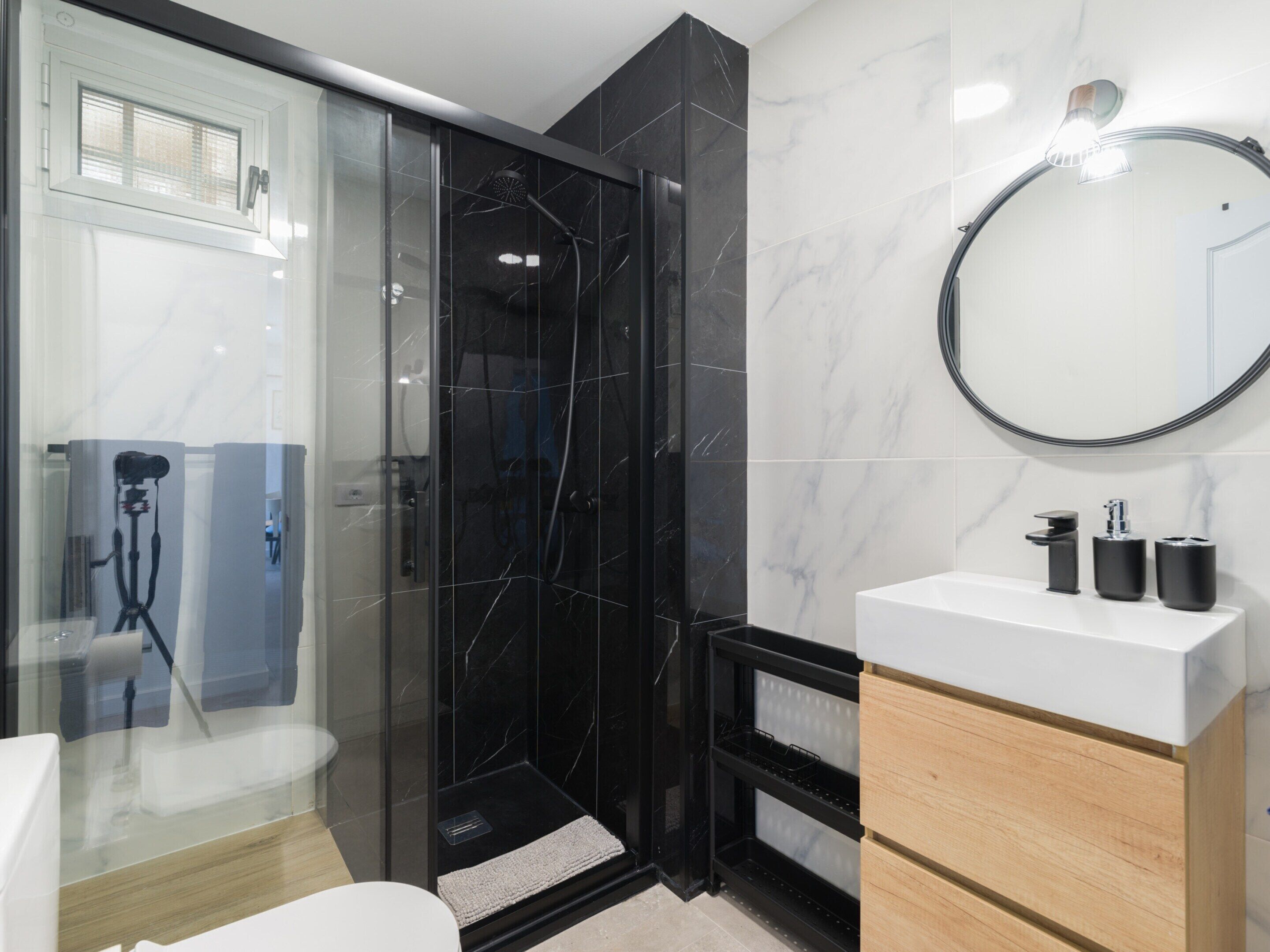 A modern bathroom with a glass-enclosed shower, a white sink with black fixtures, and a wooden vanity.