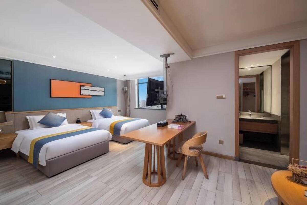 A modern hotel room with two beds, a wooden dining table, and a small seating area.