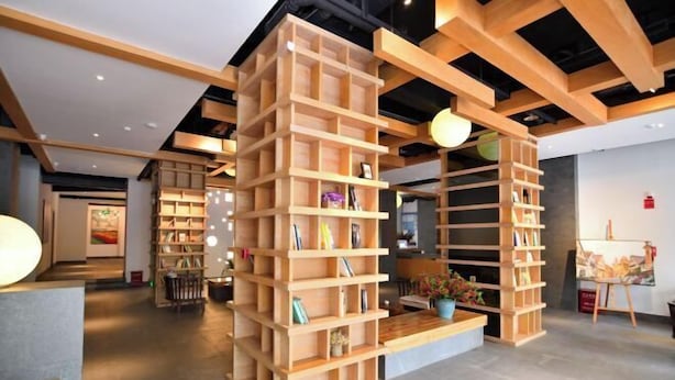 A modern interior with wooden bookshelves and a central wooden table with a potted plant. - Qifan Hotel (Kunming Railway Station Huannan South Road Metro Station Branch) (Kunming)