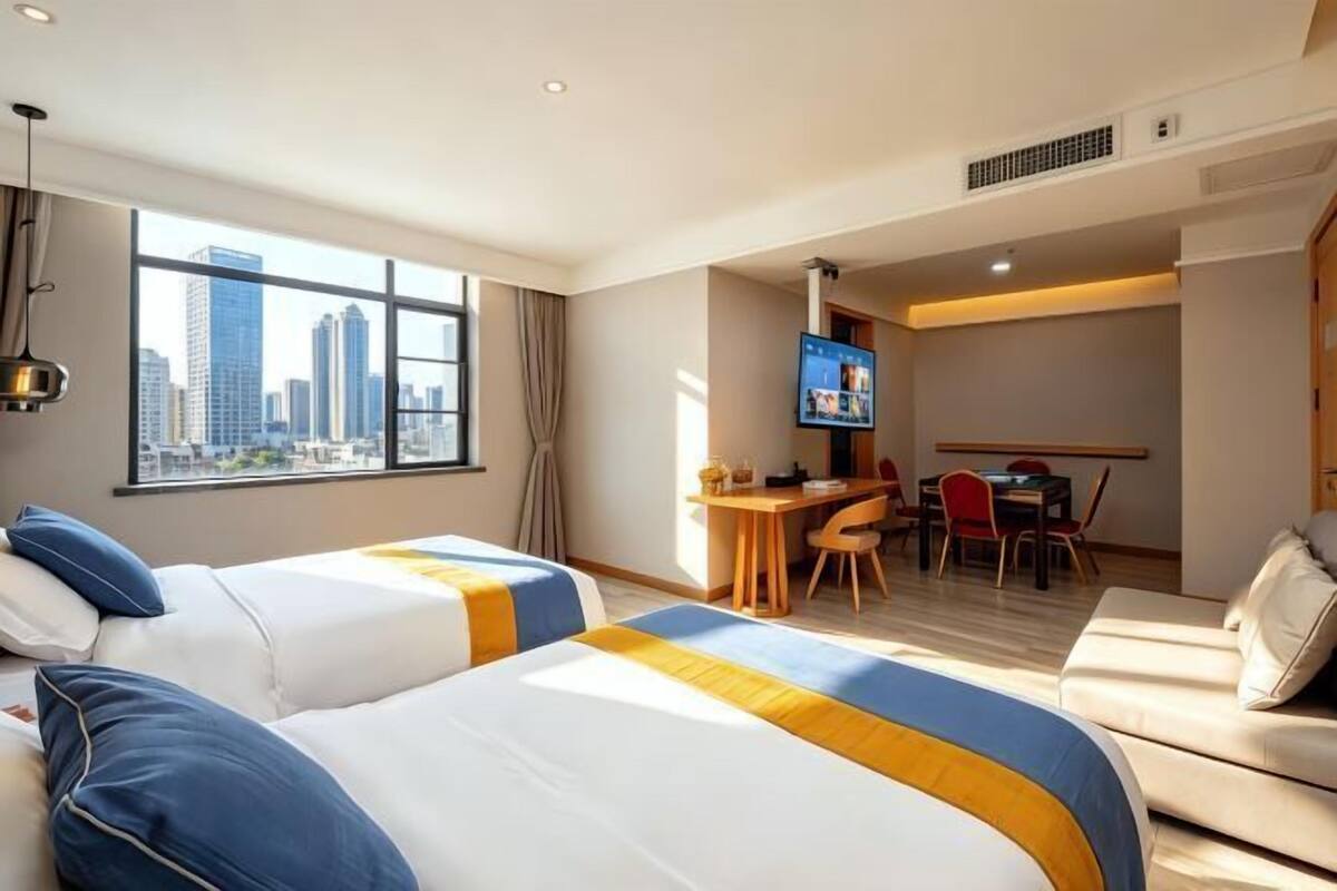 A hotel room with two beds, a desk, a TV, and a view of the city skyline.