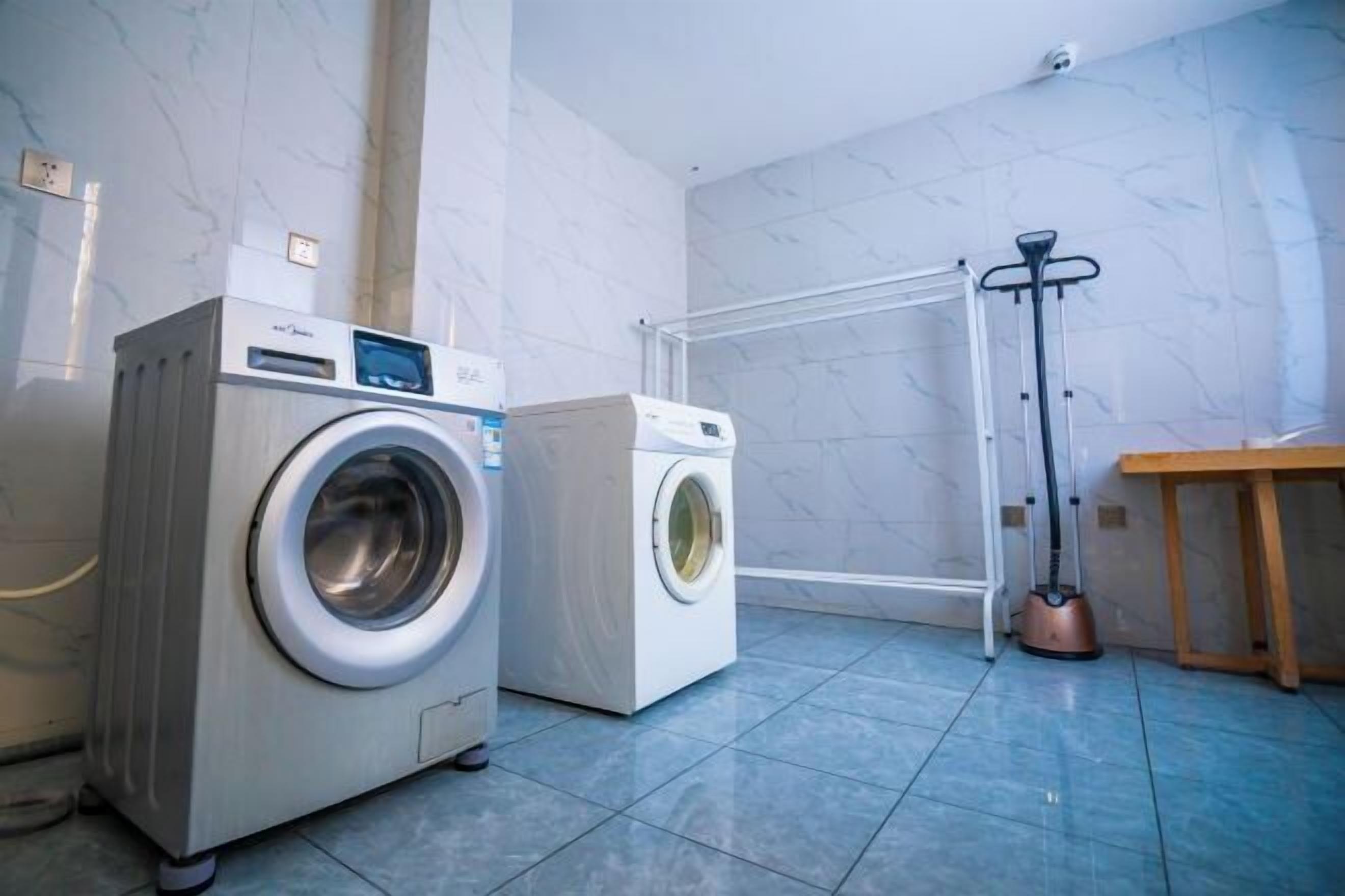 A laundry room with two front-loading washing machines, a drying rack, and a vacuum cleaner.