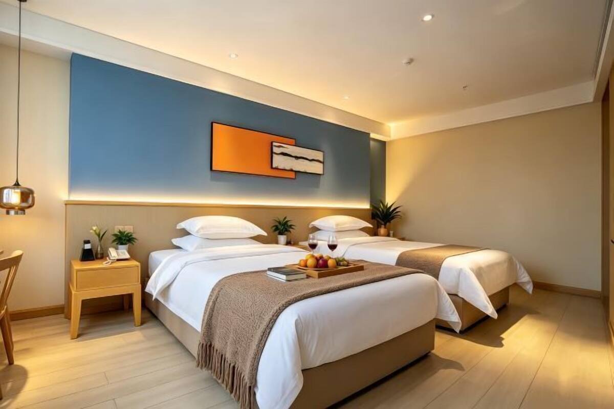 A modern hotel room with two beds, a desk, and a wall-mounted artwork.