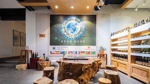 A modern interior with a central wooden table surrounded by stools, a wall with a circular emblem, and shelves with bottles. - Qifan Hotel (Kunming Railway Station Huannan South Road Metro Station Branch) (Kunming)