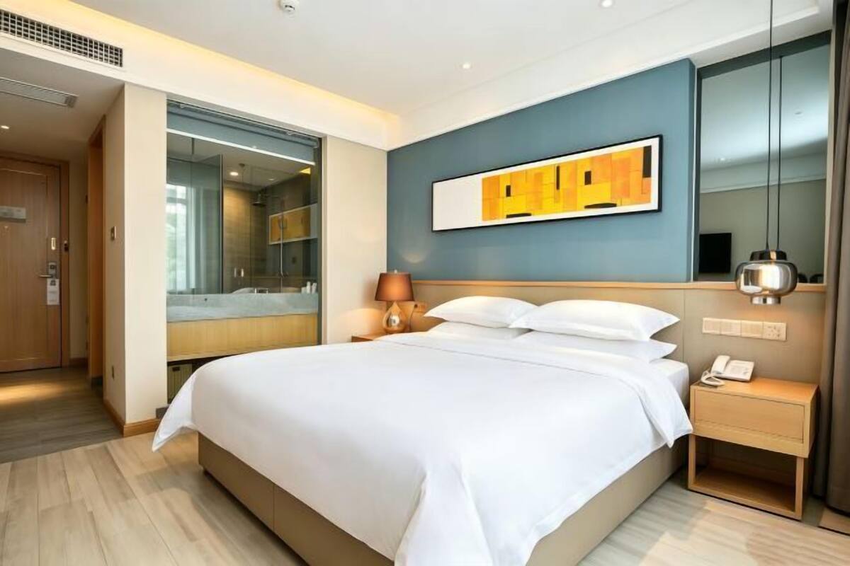 A hotel room with a large bed, a bedside table with a lamp, a phone, and a mirror.