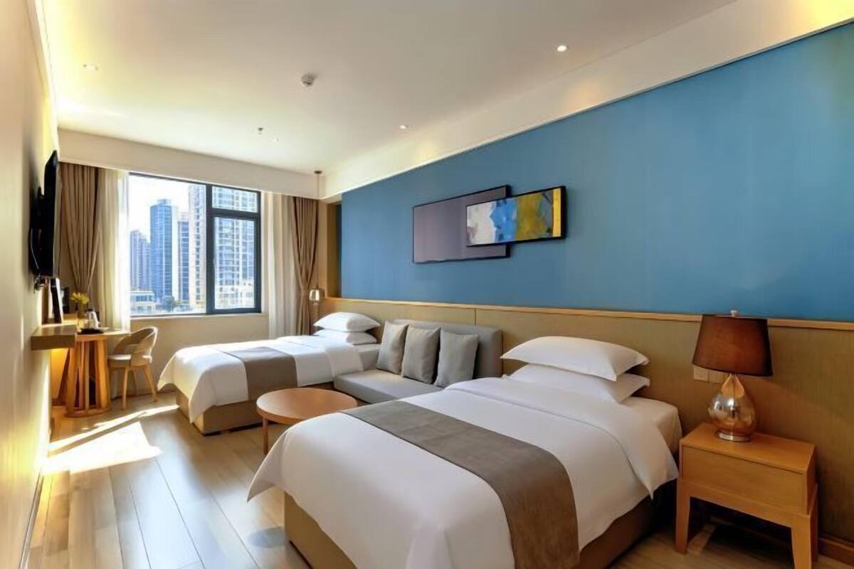 A hotel room with two beds, a desk, a chair, a TV, and a window with a city view.