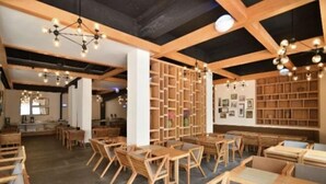 A spacious room with wooden tables and chairs, a large bookshelf, and hanging light fixtures. - Qifan Hotel (Kunming Railway Station Huannan South Road Metro Station Branch) (Kunming)