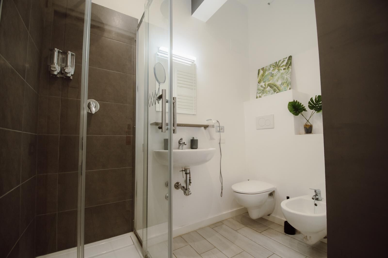 Een moderne badkamer met een glazen douchecabine, een wastafel op voet, een toilet en een douchetoilet.