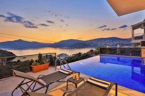 Una piscina a sfioro sul tetto con vista mare e montagne al tramonto.