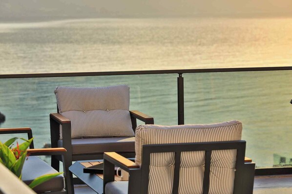 Un balcone con due sedie a righe e un tavolino, con vista su un mare calmo.