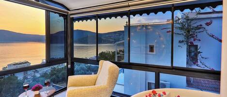A balcony with a chair and a table, overlooking a body of water and a mountainous landscape.