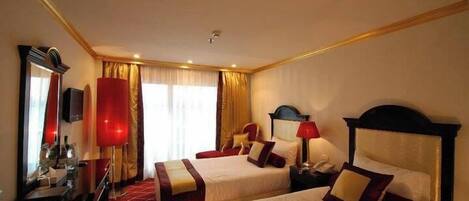 A hotel room with two beds, a desk, a mirror, and a window with curtains.