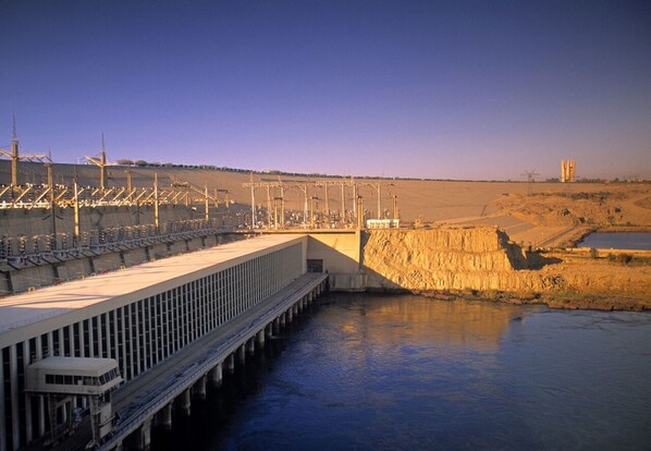 A large dam with a long spillway and multiple gates, surrounded by a dry landscape.