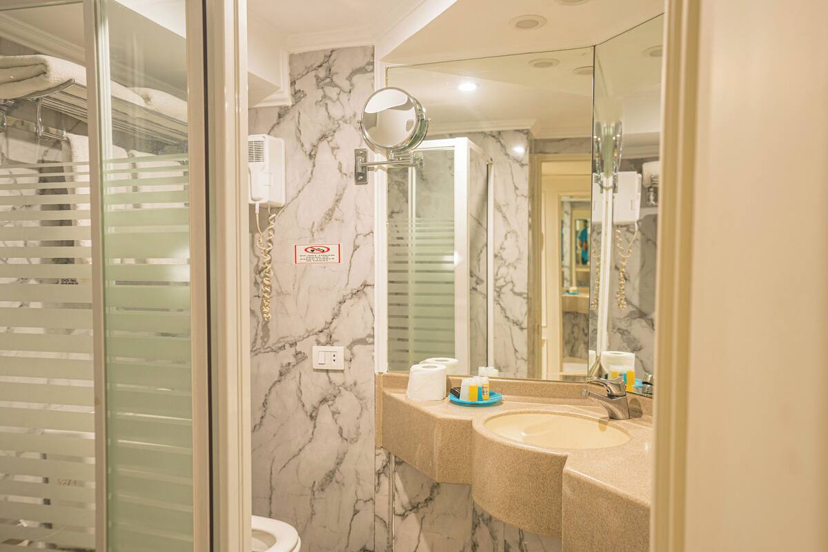 Un bagno con parete in marmo, lavabo, specchio e porta asciugamani.