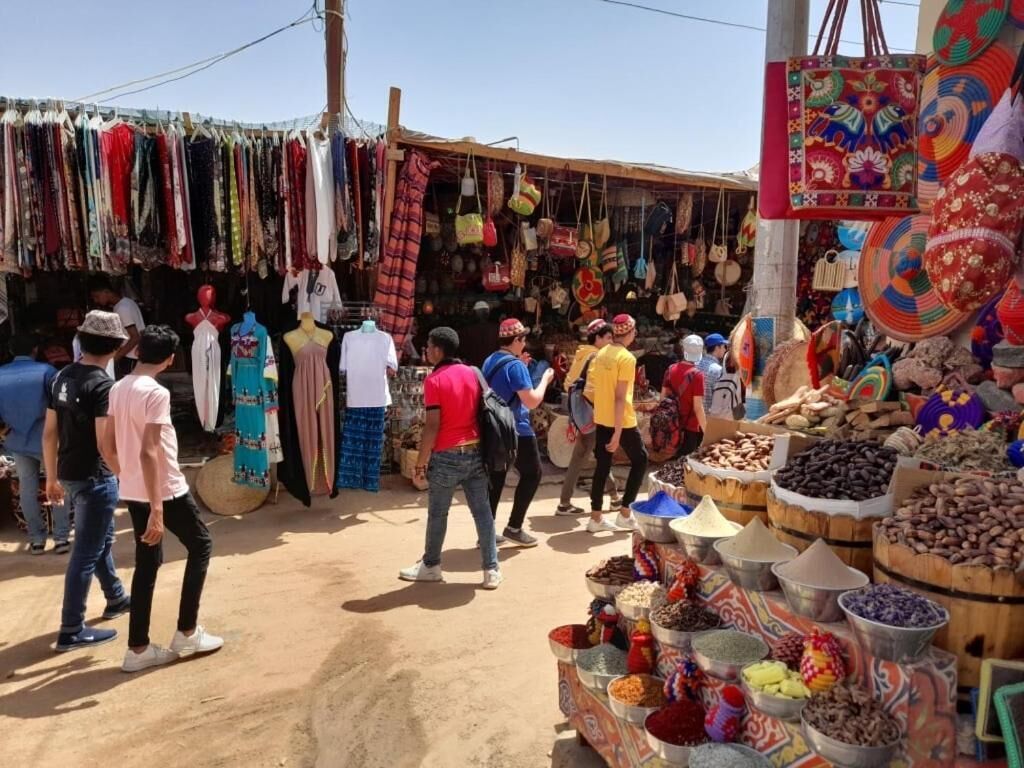 A bustling outdoor market with various stalls selling textiles, bags, and spices.