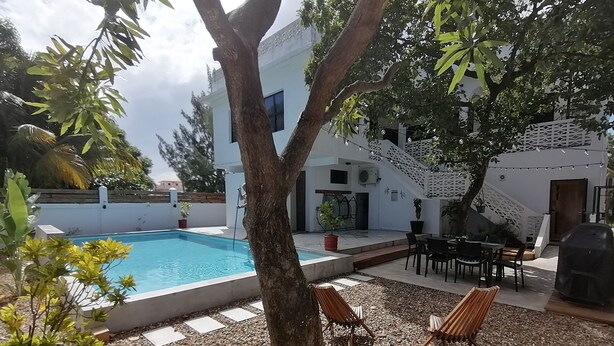 Ein Poolbereich mit Baum, Sitzgelegenheiten im Freien und einer Treppe zu einer überdachten Zone.