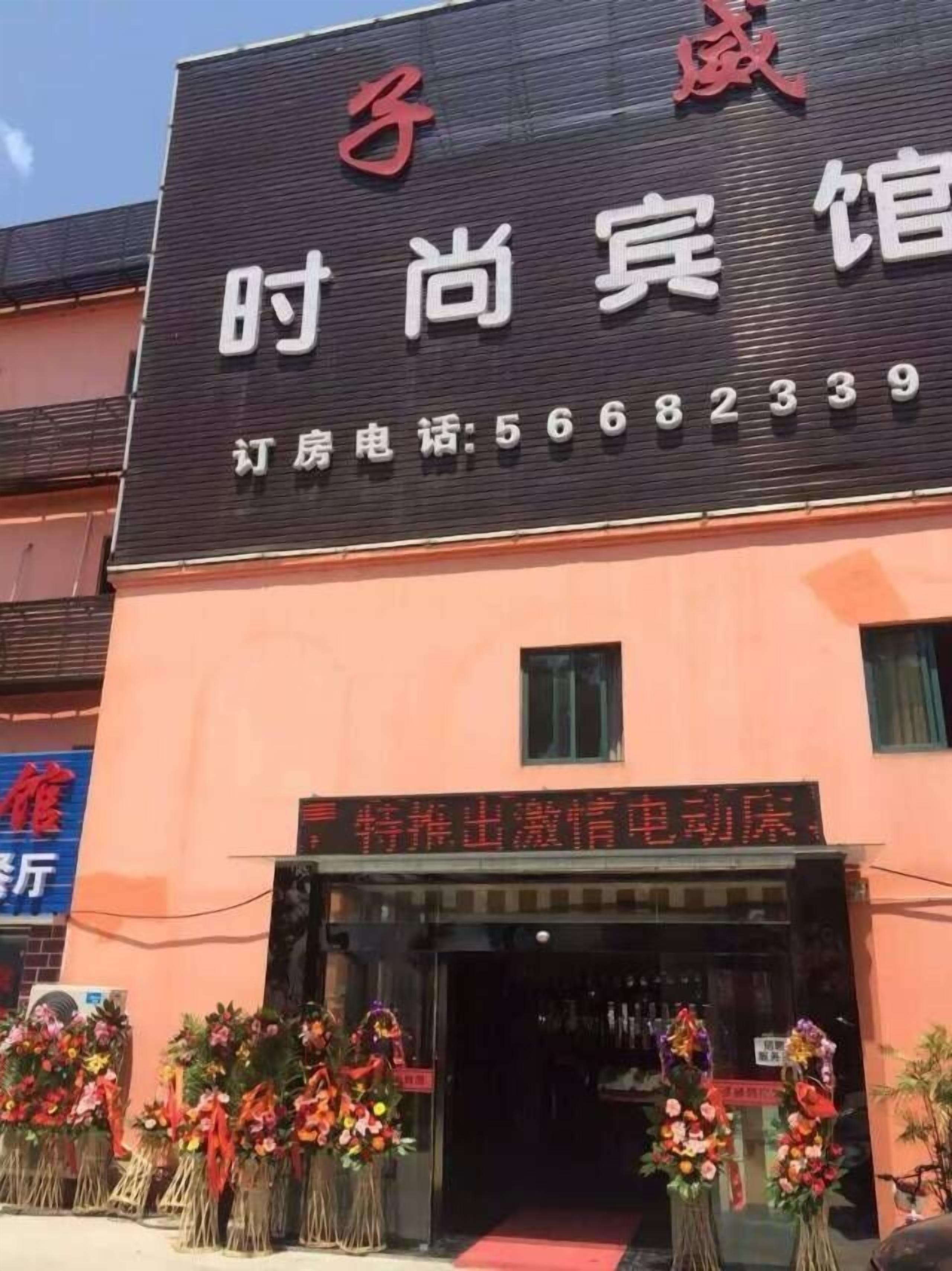 A hotel with a black facade and red signage. There are flower arrangements outside the entrance.