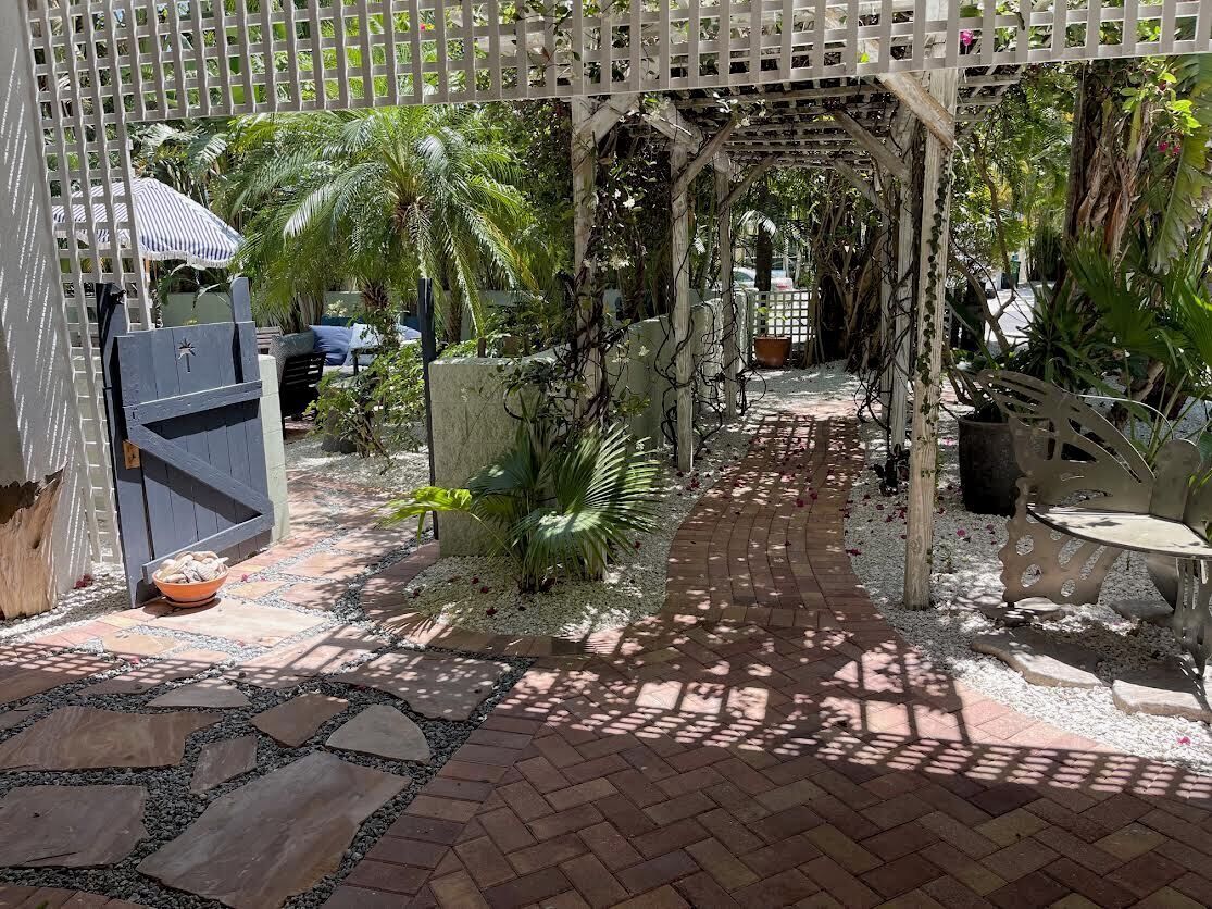 A garden pathway with a pergola, palm trees, and a stone-tiled walkway.