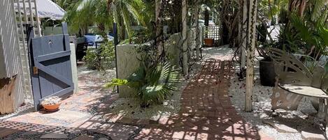A garden pathway with a pergola, palm trees, and a stone-tiled walkway.