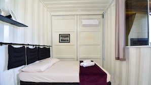 A neatly made bed with a black headboard, a white mattress, and a purple throw blanket. There is a framed picture on the wall above the bed. - Contêiner Exclusivo - Praia da Gamboa (Garopaba)