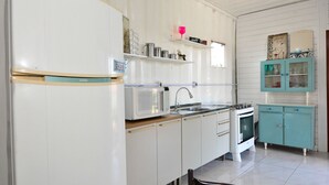 A kitchen with white cabinets, a microwave, a sink, and a stove. There are shelves with various items and a teal cabinet with glass doors. - Contêiner Exclusivo - Praia da Gamboa (Garopaba)