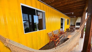 Ein gelbes Gebäude mit Holzterrasse, einer Hängematte und Holzstühlen.