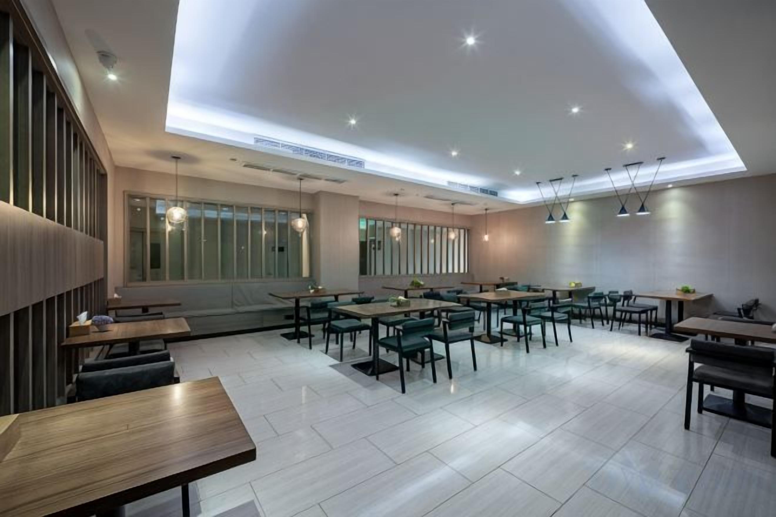 Un restaurante moderno con varias mesas y sillas, un techo alto con iluminación empotrada y amplias ventanas.