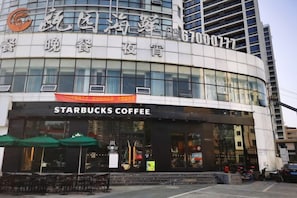 A building with a Starbucks Coffee shop on the ground floor, featuring a modern glass facade and outdoor seating area. - Rest Comfort Hotel (Wenzhou Oubei Shuangta Road) (Yongjia)