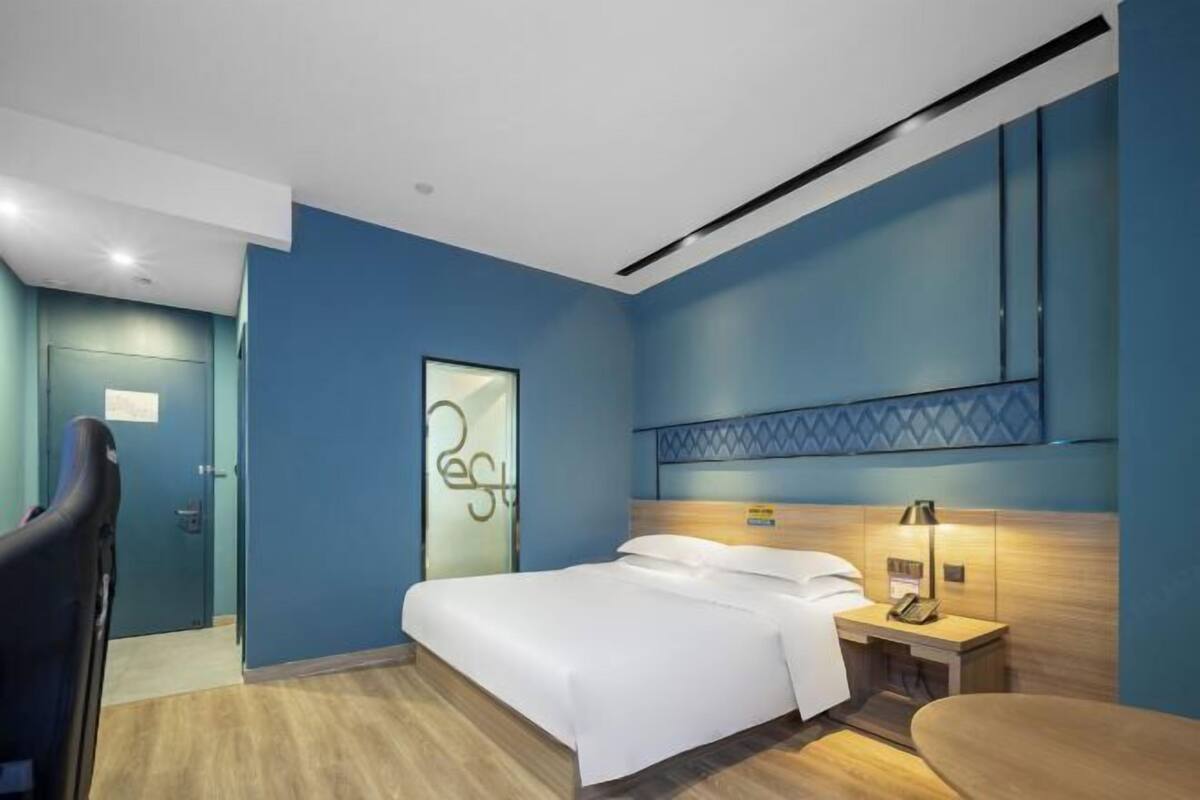 A modern hotel room with a bed, bedside table, lamp, and a door with a glass panel.