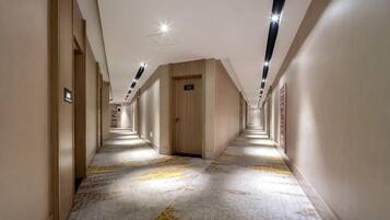 A hotel corridor with a patterned floor, wooden doors, and recessed lighting.
