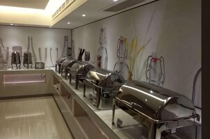 Uma área de buffet com diversas estações de serviço em aço inoxidável e um painel fixado na parede exibindo diversos utensílios de cozinha.