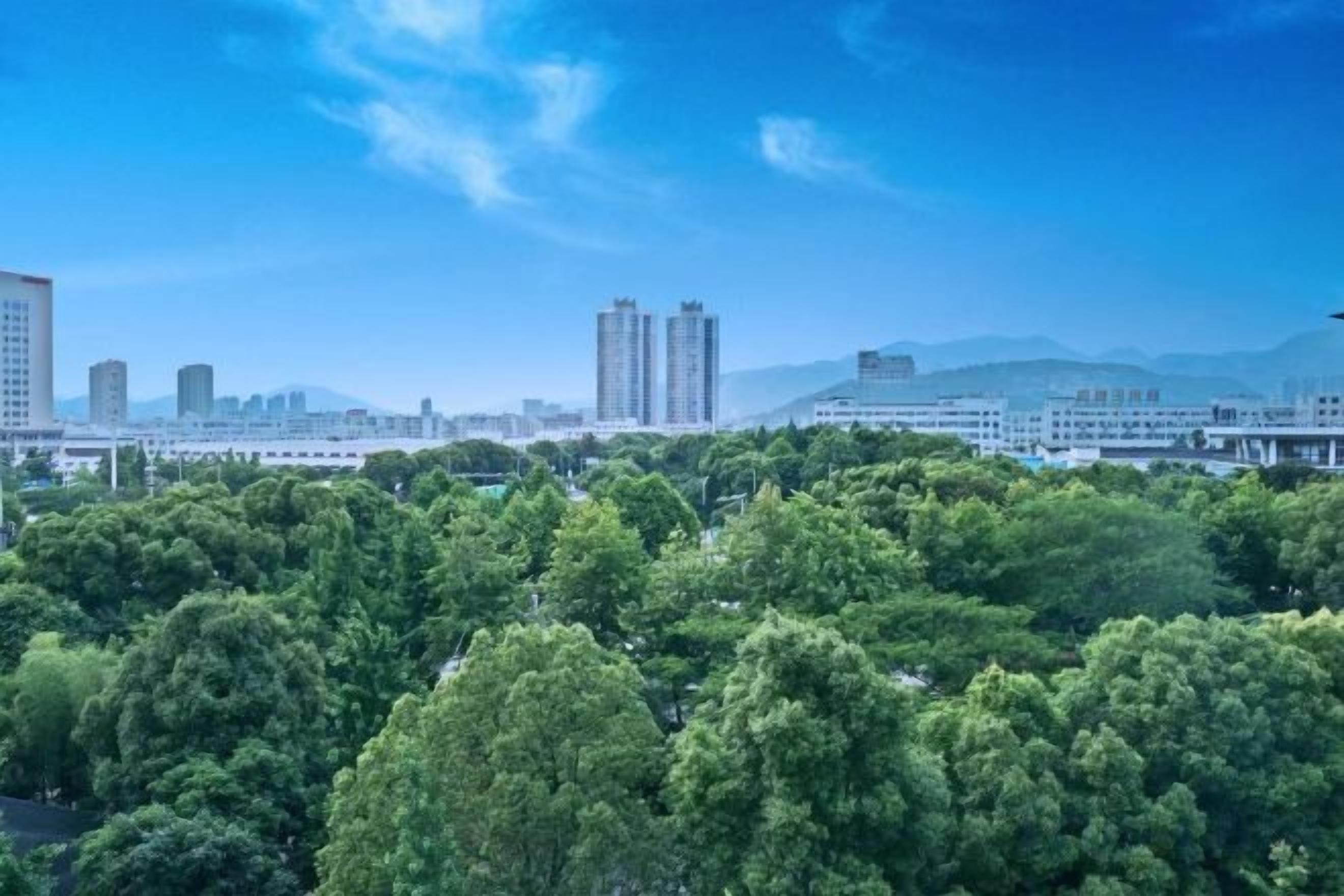 A cityscape with dense greenery in the foreground and high-rise buildings in the background.