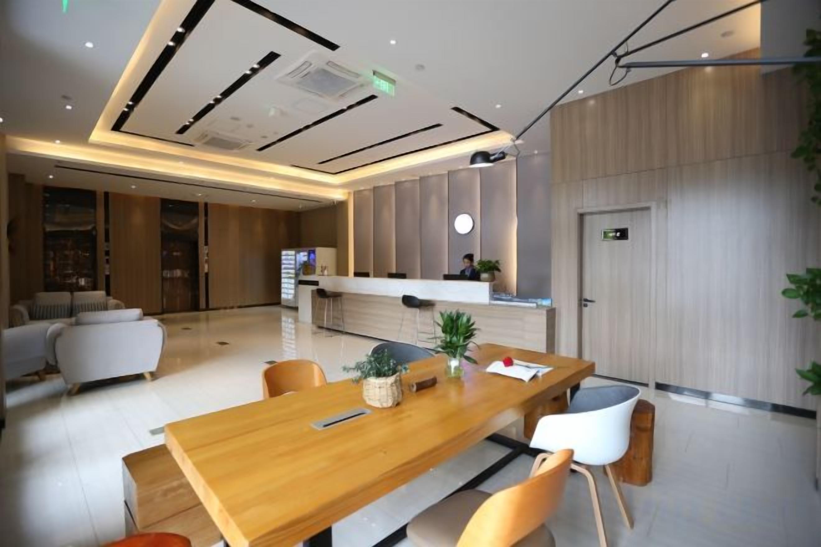 A modern hotel lobby with a reception desk, seating area, and a large wooden table.