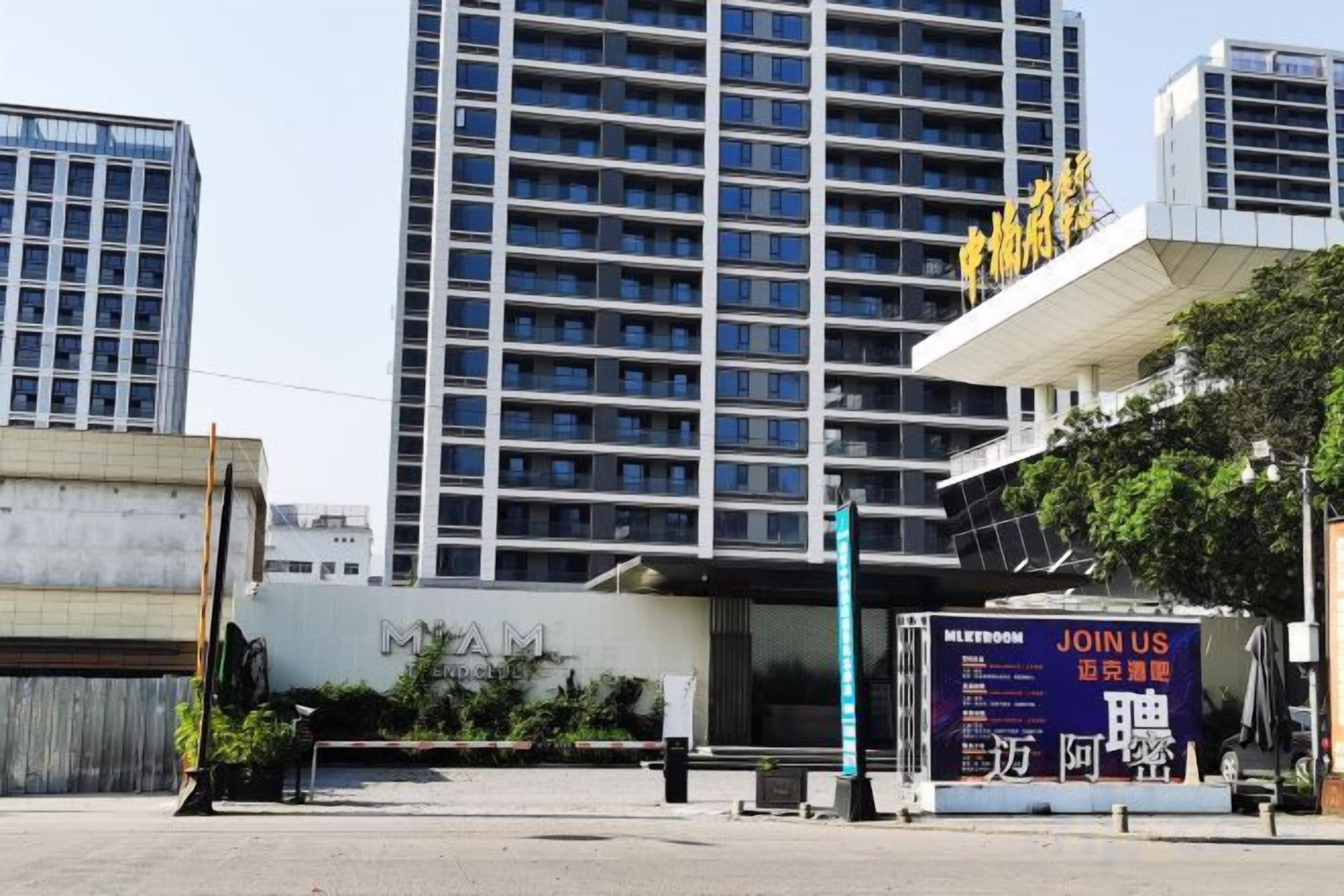 A modern building with a large glass facade, a signboard with 'JOIN US' and 'MEETROOM' text, and a clear sky.