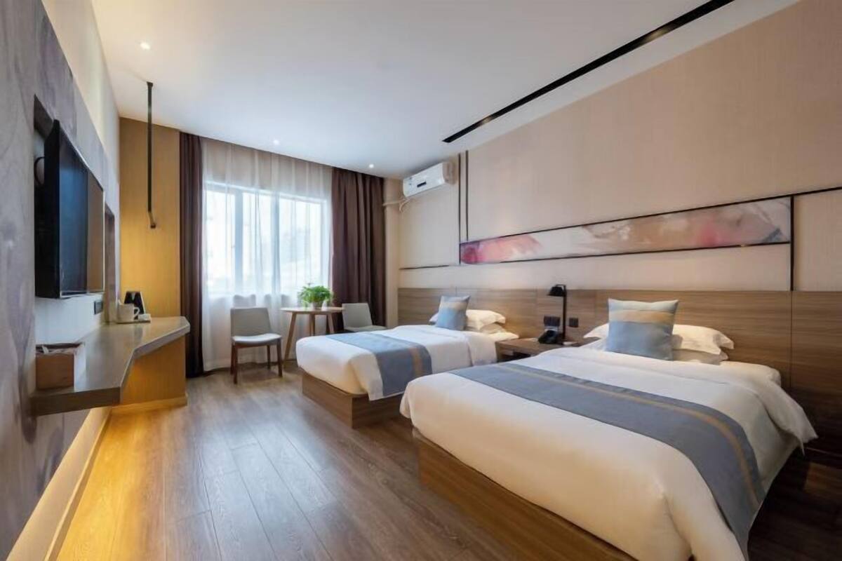 A hotel room with two beds, a desk, a chair, a TV, and a window with curtains.
