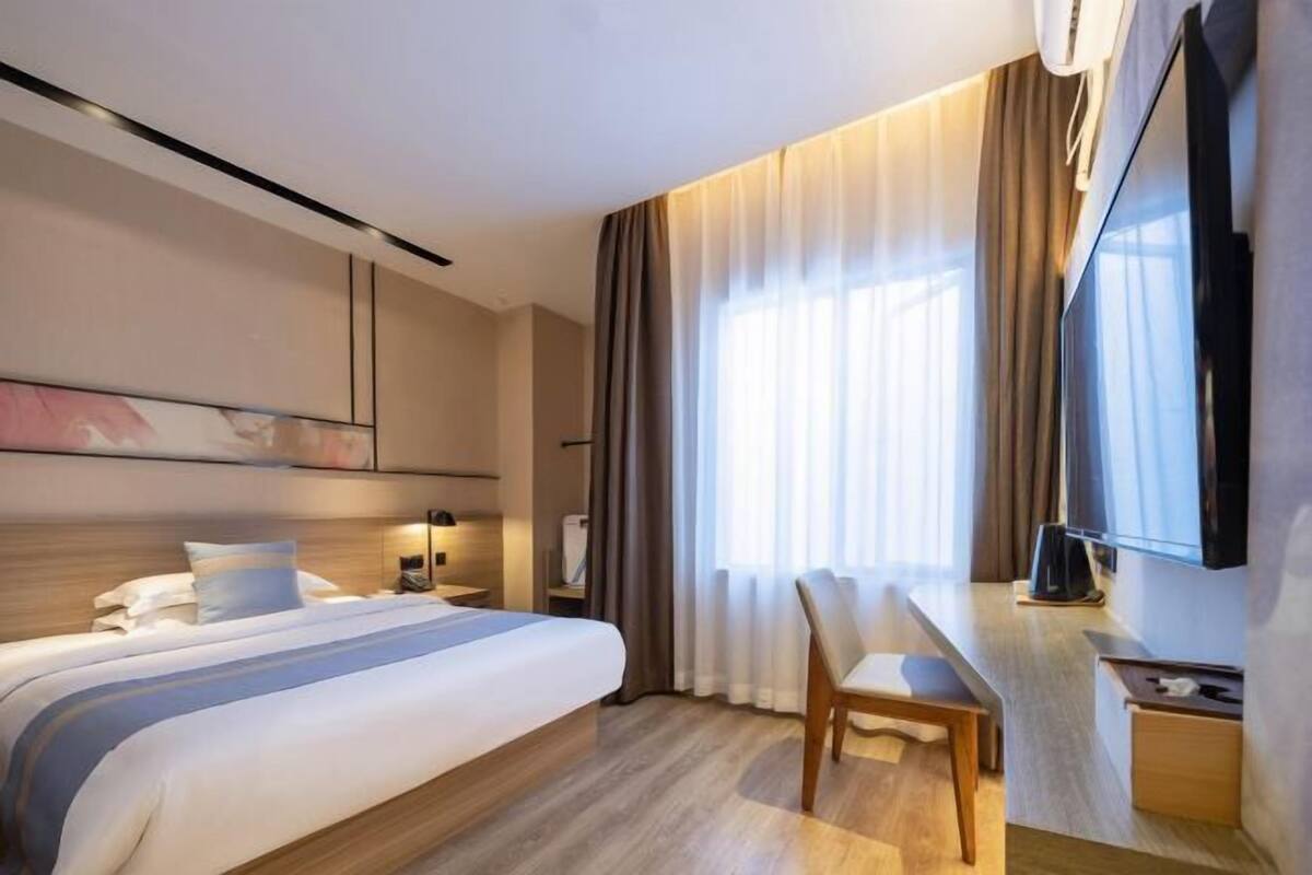 A hotel room with a bed, a desk, a chair, a TV, and a window with curtains.