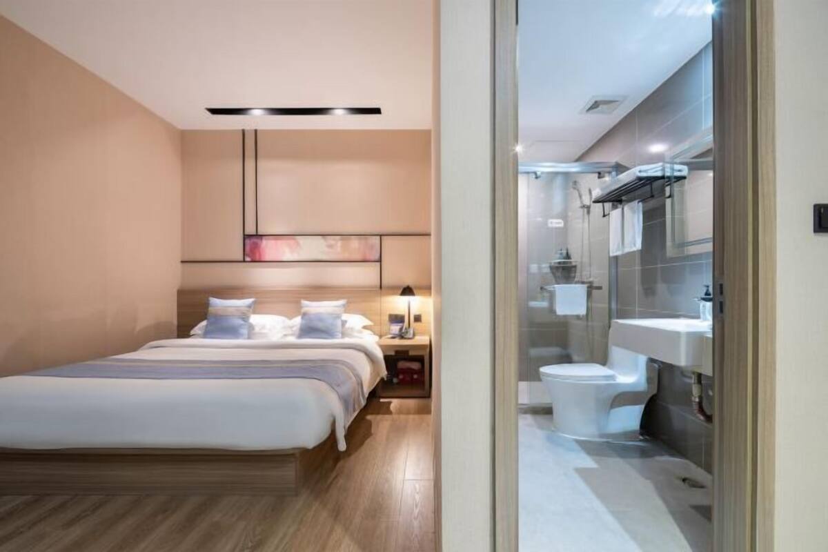 A modern hotel room with a bed, bedside table, and a view into the bathroom.