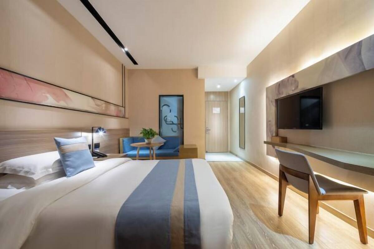 A modern hotel room with a large bed, a desk, a chair, a TV, and a small table with a plant.